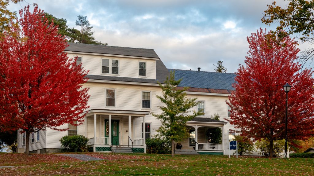 White farmhouse (The Maples) with red maple trees on the left and right.