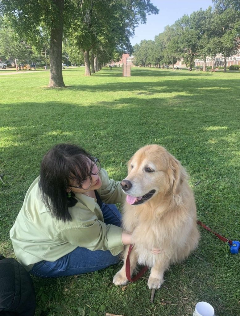 A picture of a young girl leaning over to the face of sitting golden retriever. 