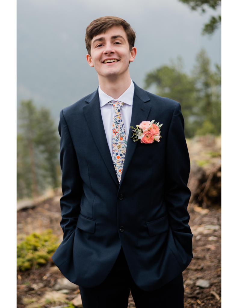 A young man, smiling, in a blue suit with a foggy mountain background.