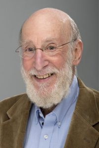 A smiling older man (Doug Allen) with a white beard and glasses in a suit.