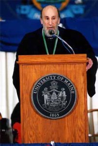 A man (Doug Allen) behind a podium delivering a commencement speech.