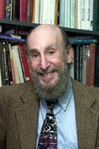 A smiling man (Doug Allen) with a beard in a suit with a bookcase background.